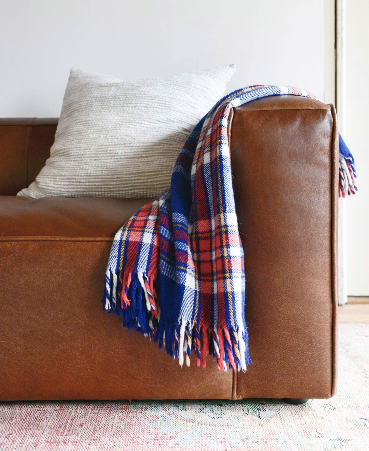 Een plaid throw is gedrapeerd over een artikel leren sofa van Yellow Brick Home